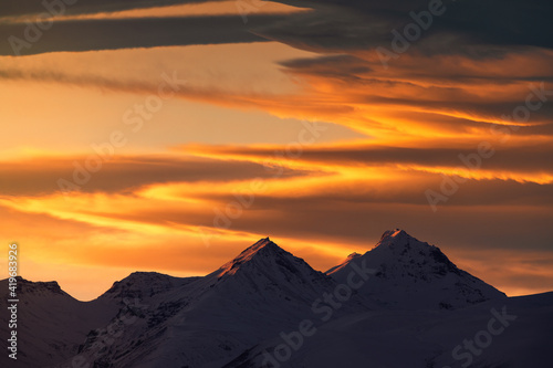  Beautiful sunset with dramatic orange clouds. The mountain peak snow-covered on the sunset. 