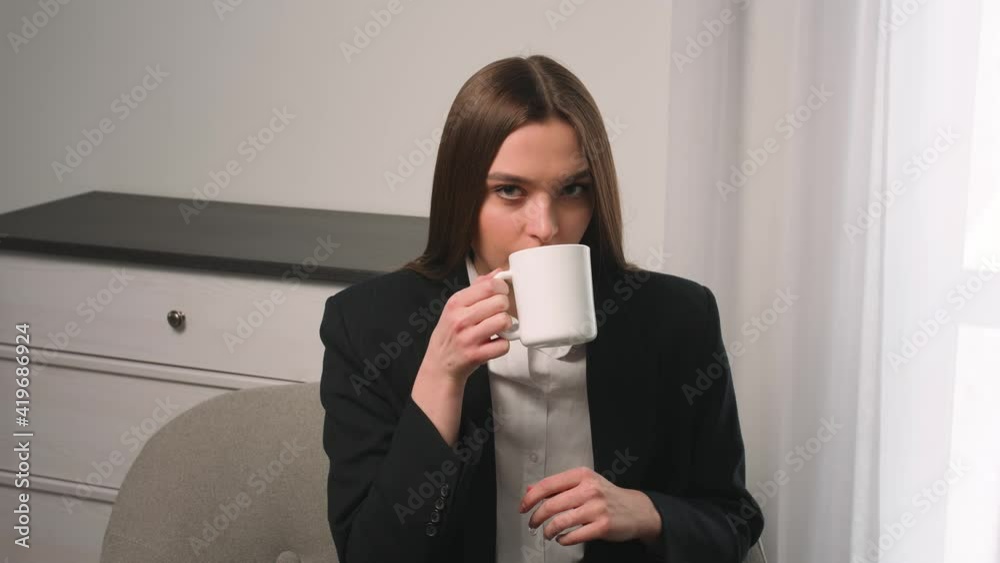 Portrait of satisfied businesswoman drinking tea at home office. Attractive woman enjoying cup of coffee at home in slow motion. Smiling woman holding cup of tea in hands at morning Portrait of satisfied businesswoman drinking tea at home office. Attractive woman enjoying cup of coffee at home in slow motion. Smiling woman holding cup of tea in hands at morning