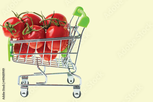 Close up view of red tomatoes in shopping cart on yellow background isolated. 