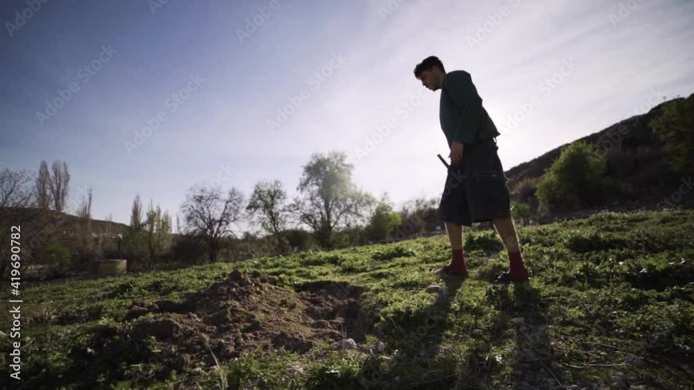 Joven agricultor cava agujero en el huerto con una azada con calidad cinematográfica a cámara lenta 