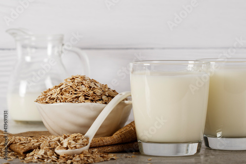 Oatmeal in a white bowl with a glass of milk on a white blue background. A healthy  nutritious morning breakfast. Oat milk. Healthy vegan non-dairy organic drink with flakes. 