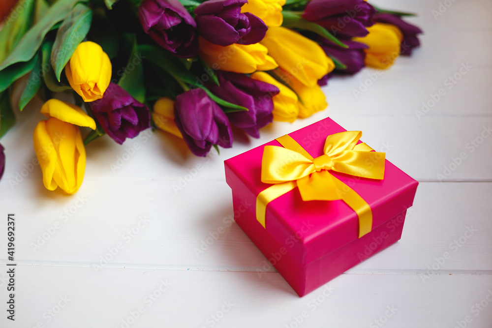 Obraz premium pink gift box with yellow bow on the background of a bouquet of tulips
