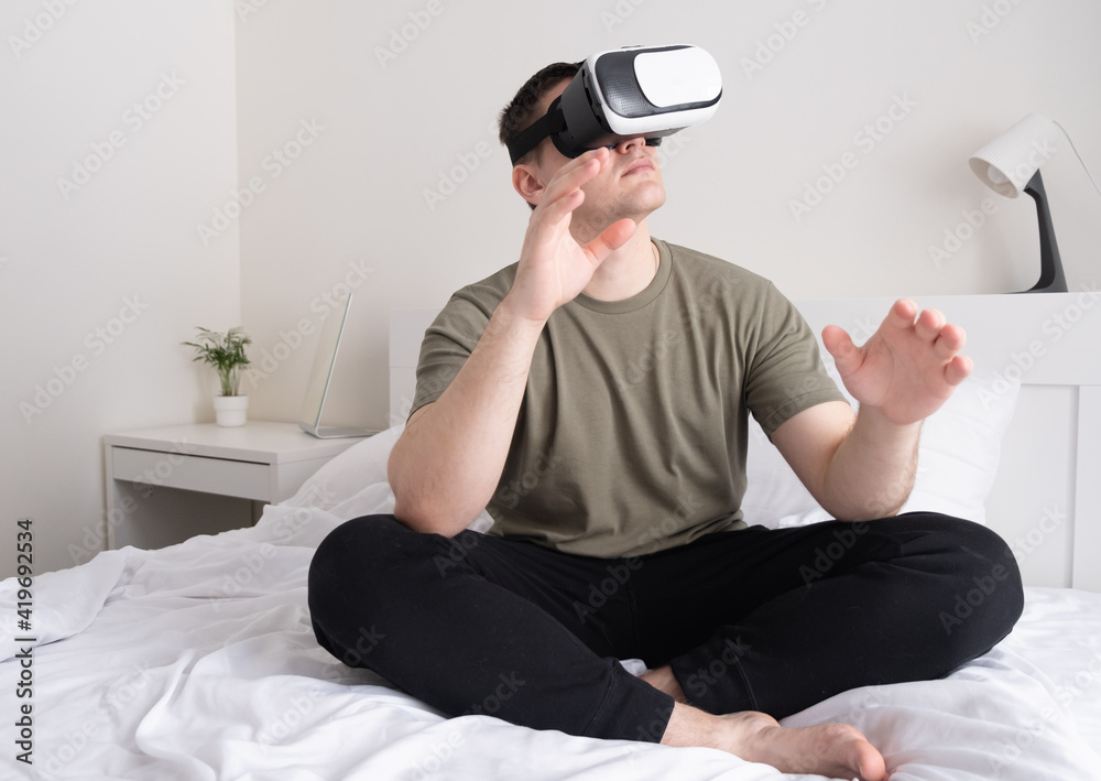 Obraz premium Man wearing virtual reality glasses. The guy sits on the bed and looks in the vr helmet
