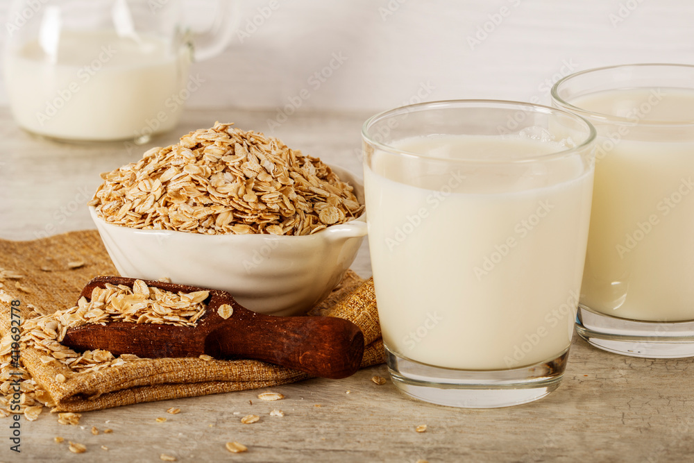 Oatmeal in a white bowl with a glass of milk on a white blue background. A healthy, nutritious morning breakfast. Oat milk. Healthy vegan non-dairy organic drink with flakes. Oatmeal in a white bowl with a glass of milk on a white blue background. A healthy, nutritious morning breakfast. Oat milk. Healthy vegan non-dairy organic drink with flakes.