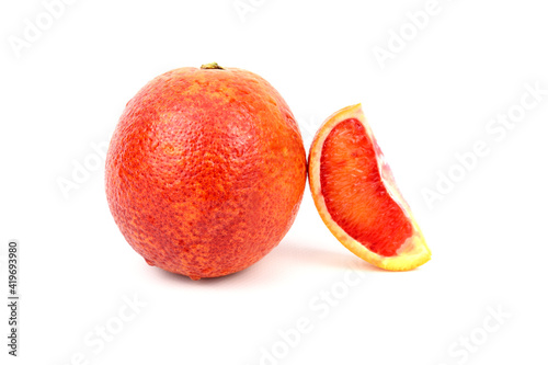 Red ripe orange. Nearby lies a slice from another orange, which rests on the first one.