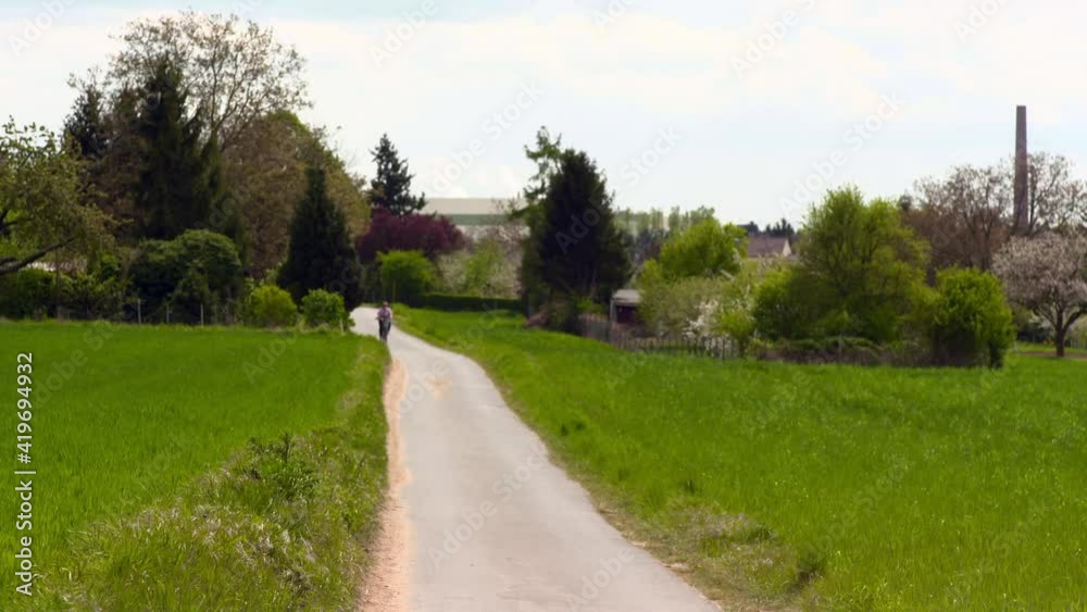 Person Rides A Bike Slowly Along A Narrow Track Running Through Grassy Field And Picturesque Trees Person Rides A Bike Slowly Along A Narrow Track Running Through Grassy Field And Picturesque Trees