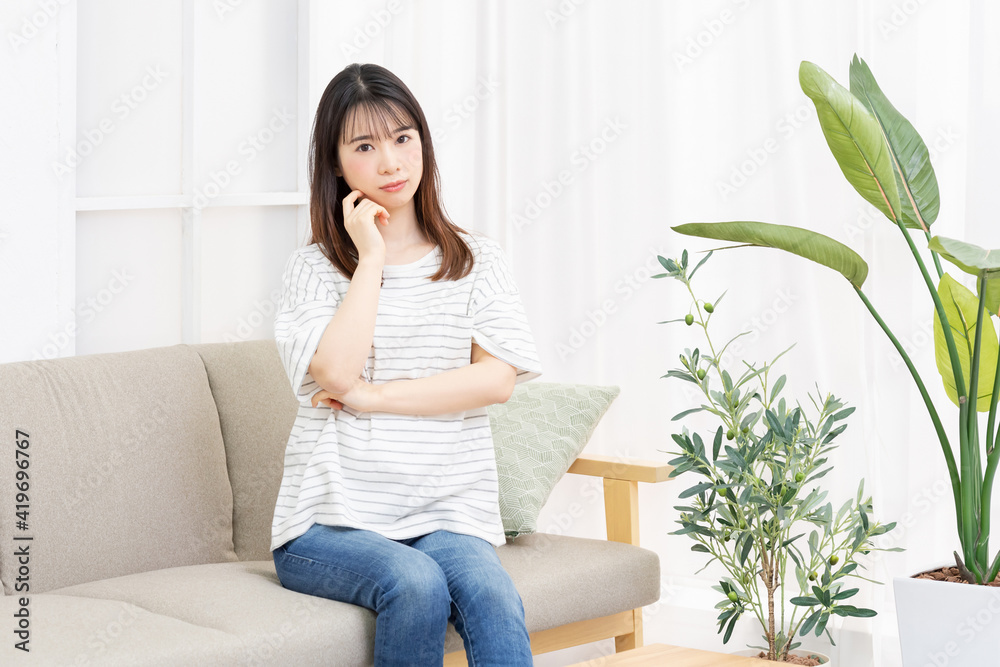 部屋のソファーに座って考え事をする若い女性 部屋のソファーに座って考え事をする若い女性