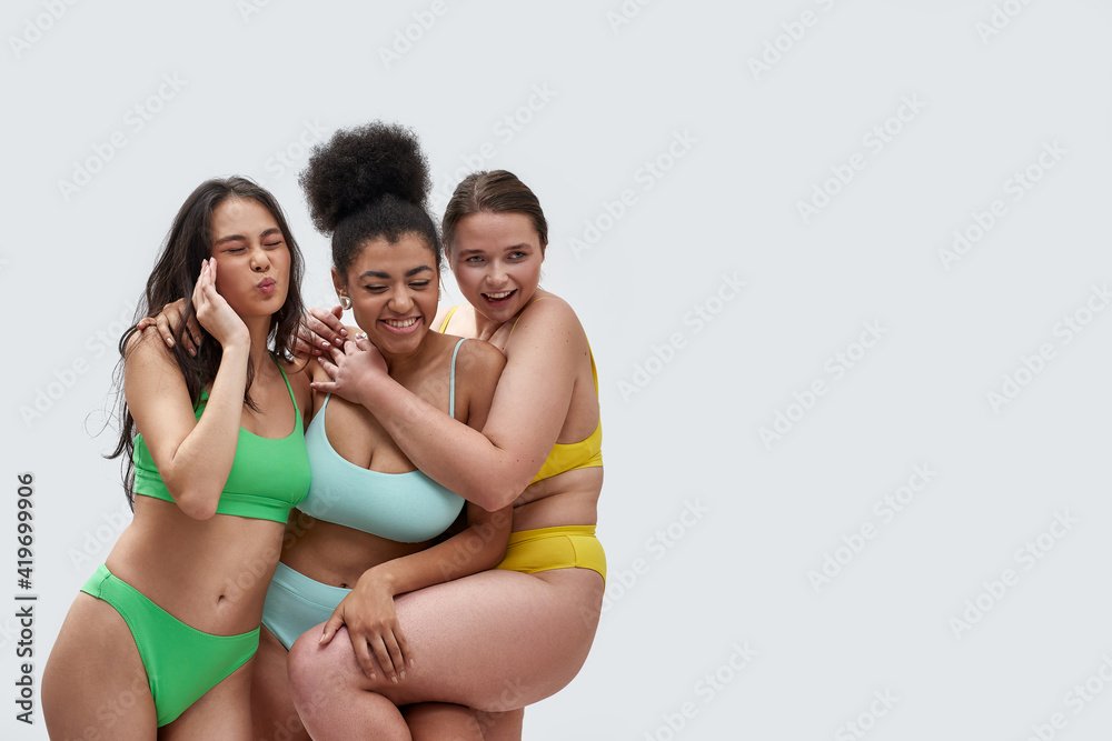 Three multiethnic young women in colorful underwear looking happy, having  fun while posing together isolated over white background Stock Photo