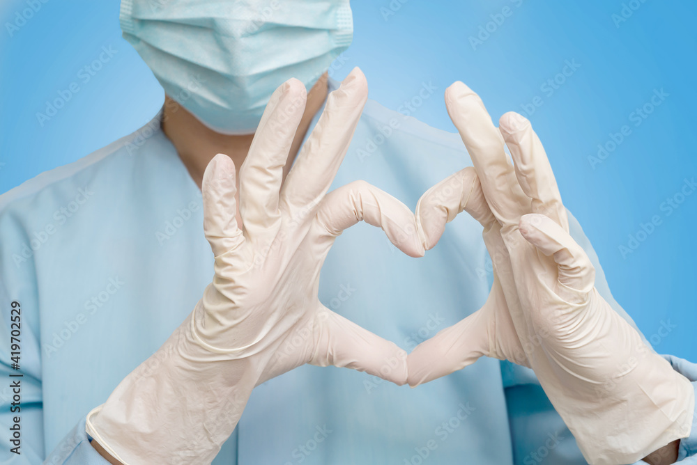 a doctor in a protective mask and gloves shows the heart with his hands. the cardiologist shows the heart sign a doctor in a protective mask and gloves shows the heart with his hands. the cardiologist shows the heart sign