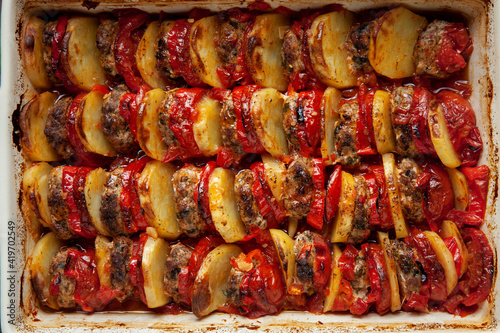 Close-up view of baked in layers and rows slices of meatballs, potatoes, tomatoes and peppers. Food background texture.