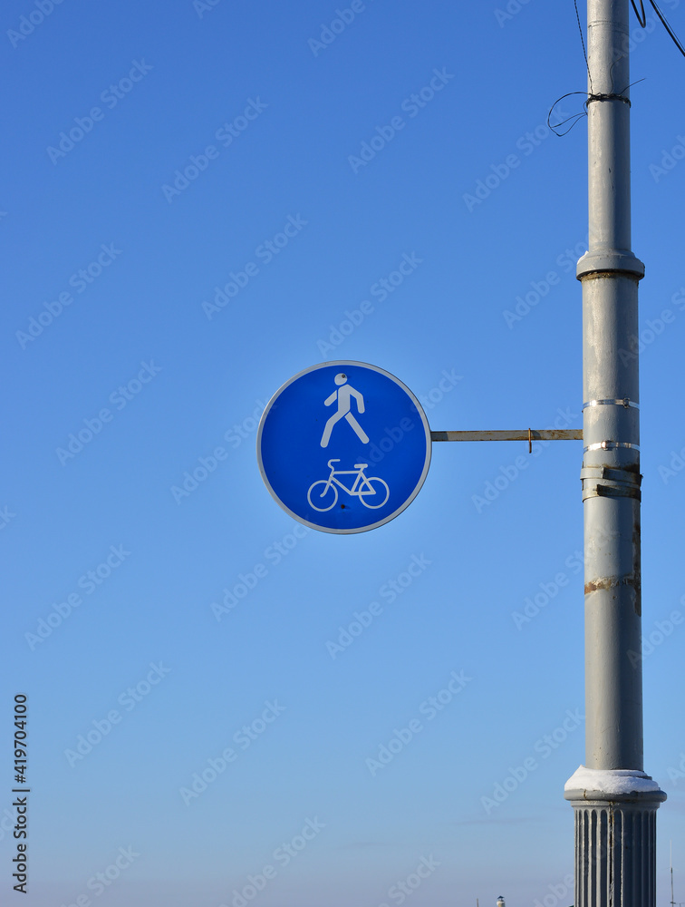 there is a bicycle and pedestrian road sign hanging on the street post, winter sunny day. blue sky background there is a bicycle and pedestrian road sign hanging on the street post, winter sunny day. blue sky background