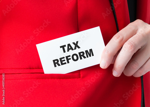 Tax Reforms text on a card in the businessman's hands, which he places in the pocket of his red jacket. Business concept