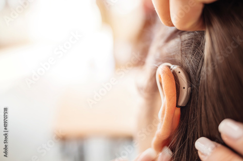Woman adjusting hearing aid indoors. Close up of a hearing aid on the woman's ear. Deaf woman wearing hearing aid. Digital hearing aid in woman's ear photo