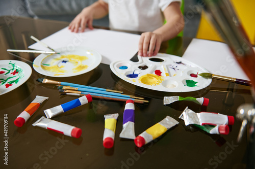 Multi-colored tubes with paints and a palette lying on a glass table.
