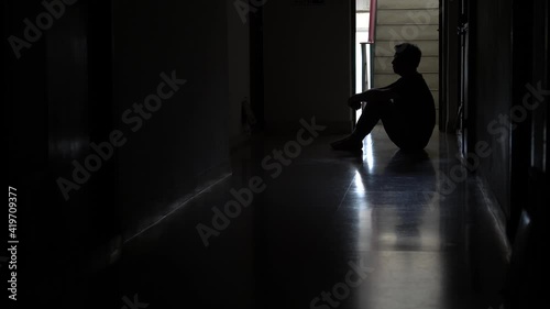 Silhouette of a stressed man sitting in the dark leaning against the wall, Stress, violence, The concept of depression and suicide.
