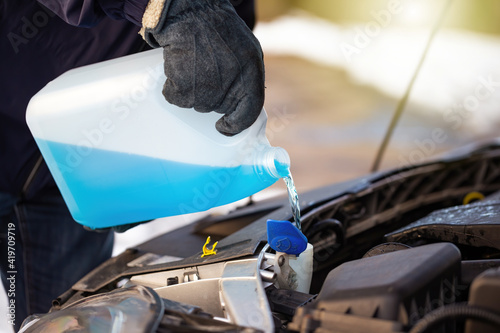 Obraz na płótnie Man filling antifreeze coolant for cleaning front window with snow in background