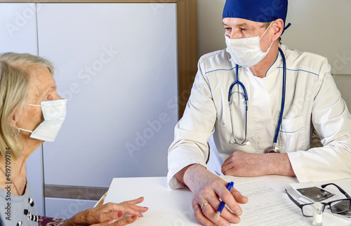 Friendly geriatrician explaining prescription for senior female patient at clinic photo