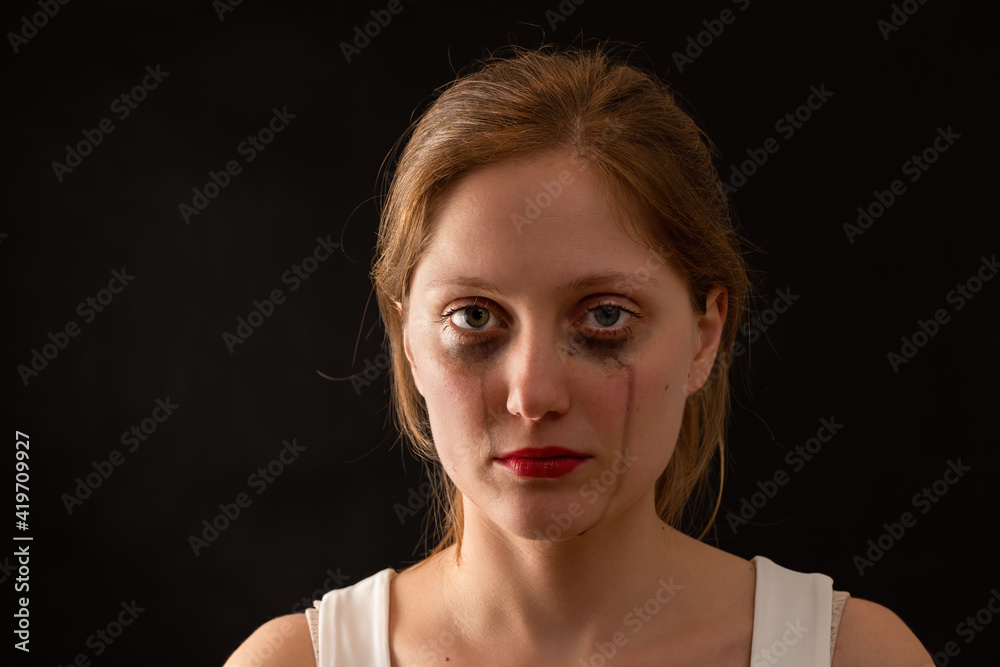 Blonde female with sad expression from front on black background. Young woman crying with blank look in darkenss. Upset female without smile in depression.