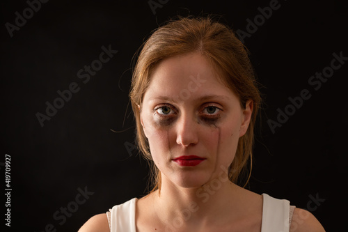 Obraz na płótnie Blonde female with sad expression from front on black background. Young woman crying with blank look in darkenss. Upset female without smile in depression. w salonie