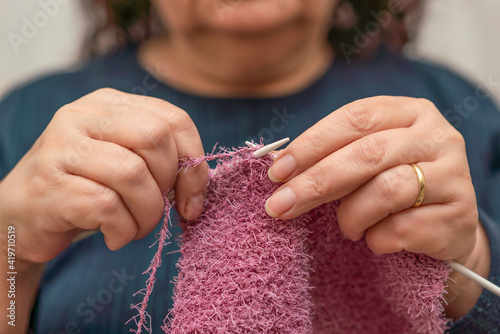 Close up of elderly woman hold knitting needles and knit a warm sweater. Yarn for knitting. Women's needlework. Knitting as a hobby for senior ladies during coronavirus pandemic.