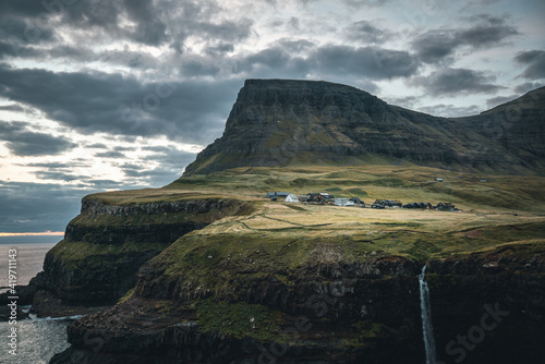 Gasadalur village and Mulafossur its iconic waterfall during sunset in summer with bluw sky. Vagar, Faroe Islands, Denmark. Rough see in the north atlantic ocean.