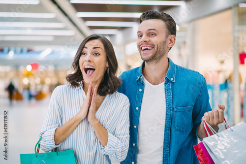 Excited young couple with shopping bags in hands are looking at the showcase while standing in the mall