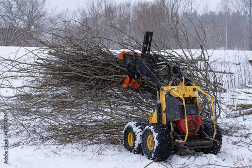 small stand-on mini skid steer with grapple full of wooden branches