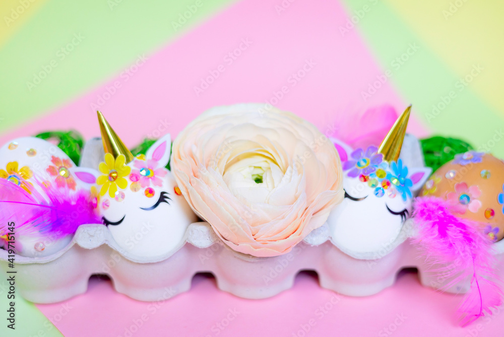 white Easter eggs decorated in the form of unicorns on a colorful background with ranunculus flowers, a minimal creative concept of a happy Easter