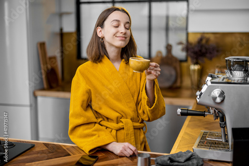 Woman in yellow bathrobe enjoying coffee during a morning routine on the stylish kitchen at home. Home coziness concept.