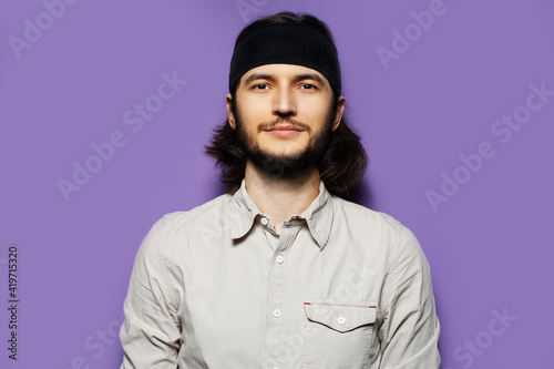 Studio portrait of young brunette guy, with long hair and confident attitude. On the background of purple wall.