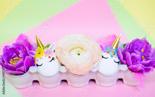 white Easter eggs decorated in the form of unicorns on a colorful background with ranunculus flowers  a minimal creative concept of a happy Easter