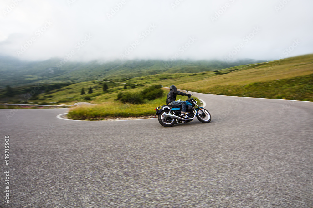 Motorcycle driver riding on mountain highway, Dolomites, central Europe.