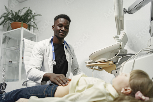 Teenager on the couch. African doctor makes an ultrasound diagnosis. Man in a white coat.