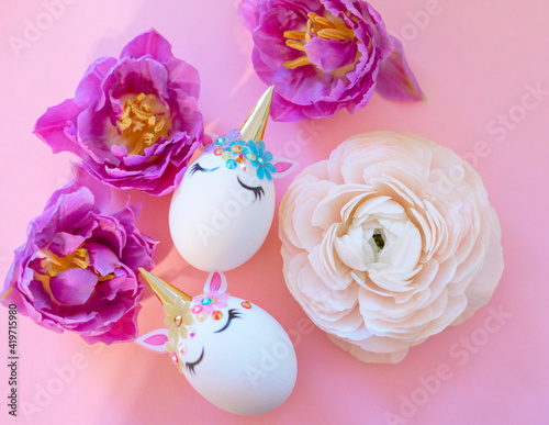 white Easter eggs decorated in the form of unicorns on a colorful background with ranunculus and tulips flowers, a minimal creative concept of a happy Easter