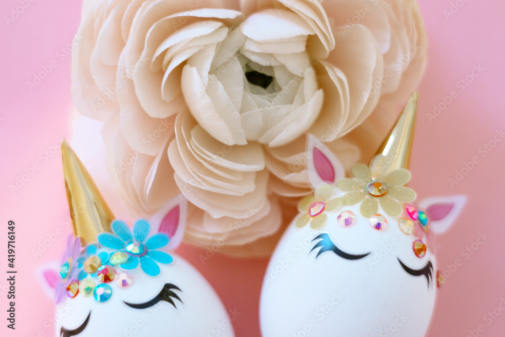 white Easter eggs decorated in the form of unicorns on a pink background with ranunculus flower, a minimal creative concept of a happy Easter white Easter eggs decorated in the form of unicorns on a pink background with ranunculus flower, a minimal creative concept of a happy Easter