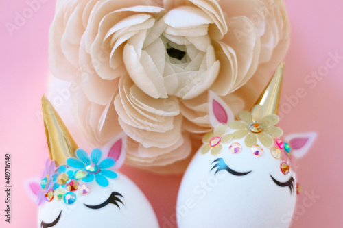 white Easter eggs decorated in the form of unicorns on a pink background with ranunculus flower  a minimal creative concept of a happy Easter