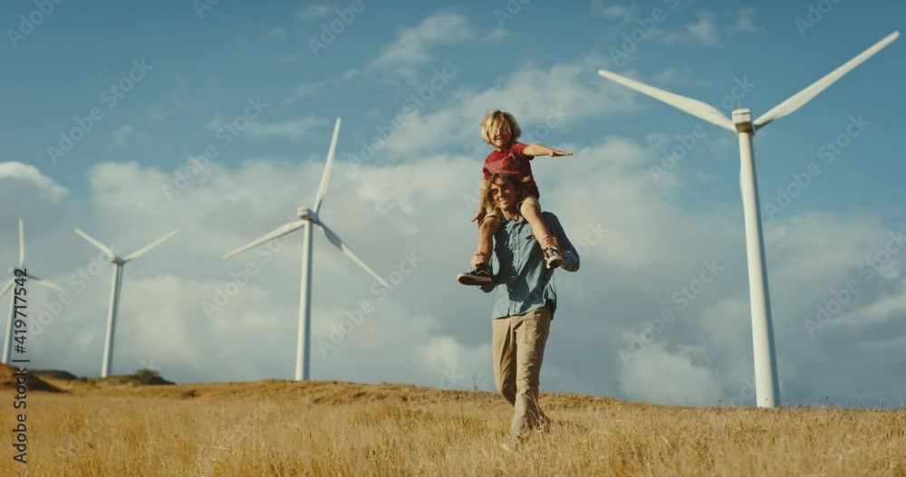 Father with young son on his back looking out at windmills on the hillside at sunset, cleaner and sustainable future, climate change, father and son bonding