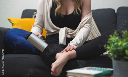 Woman massaging feet with massage percussion device at home. © M-Production