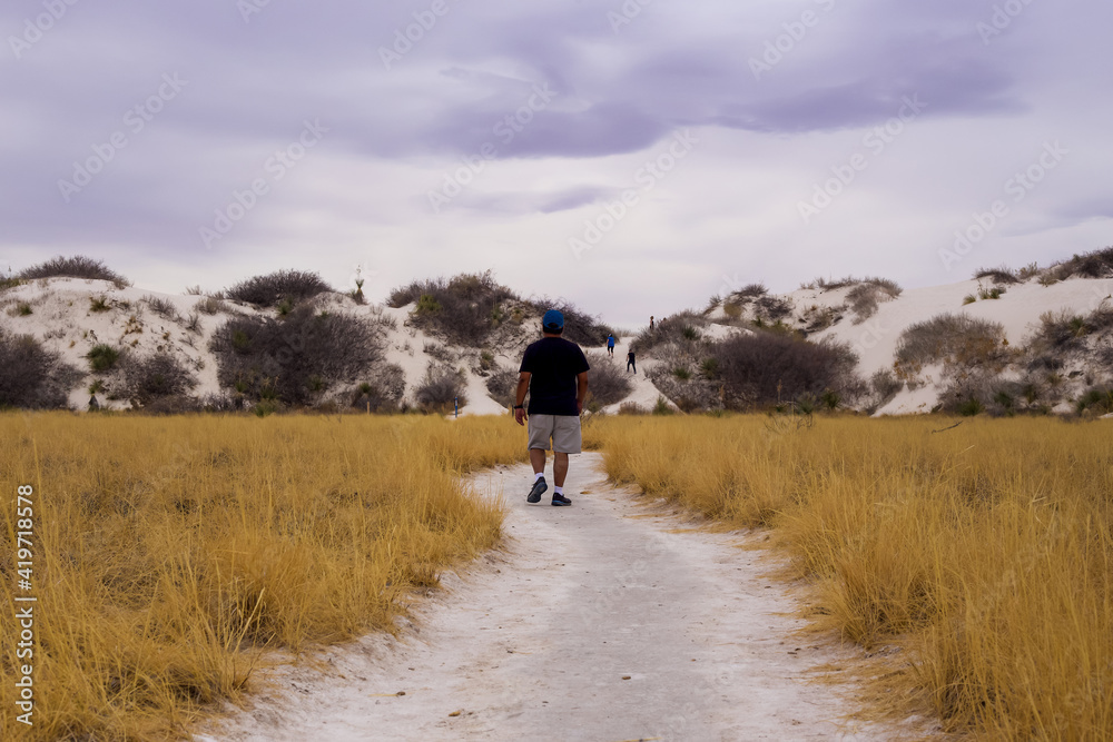 An Asian man walks towards the gypsum sand dunes on the Dune Life Nature Trail at White Sands National Park in New Mexico.