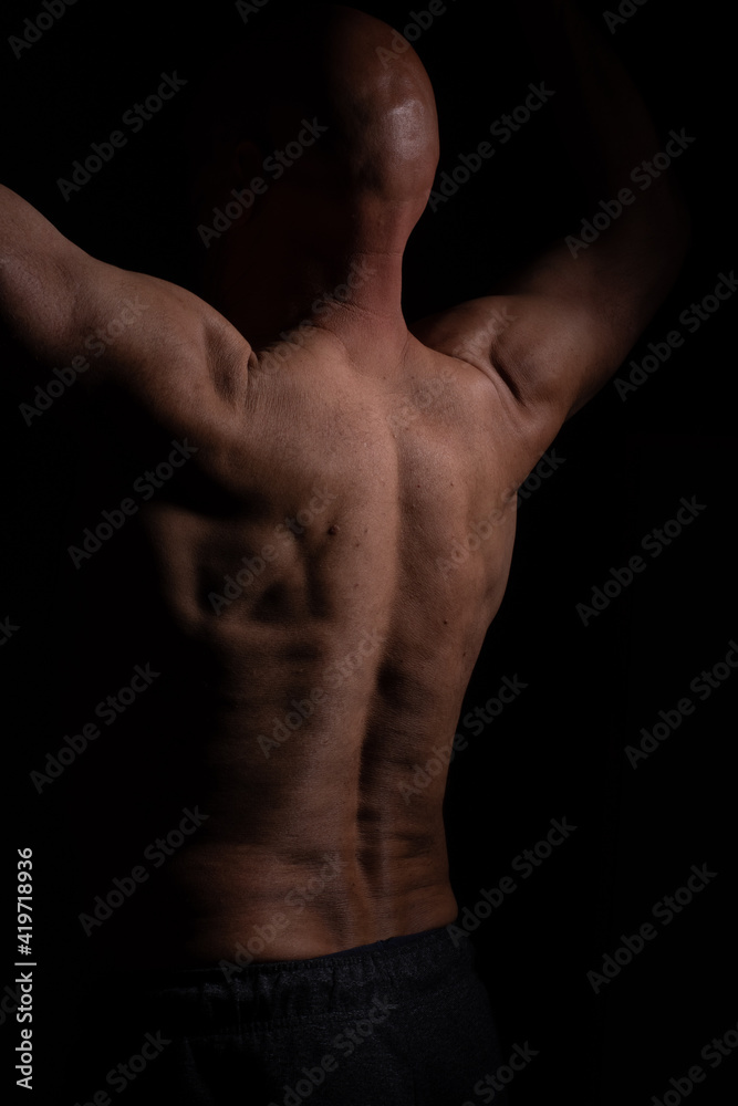 Half naked muscular man with hands up and bold head on black background
