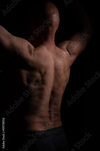 Half naked muscular man with hands up and bold head on black background
