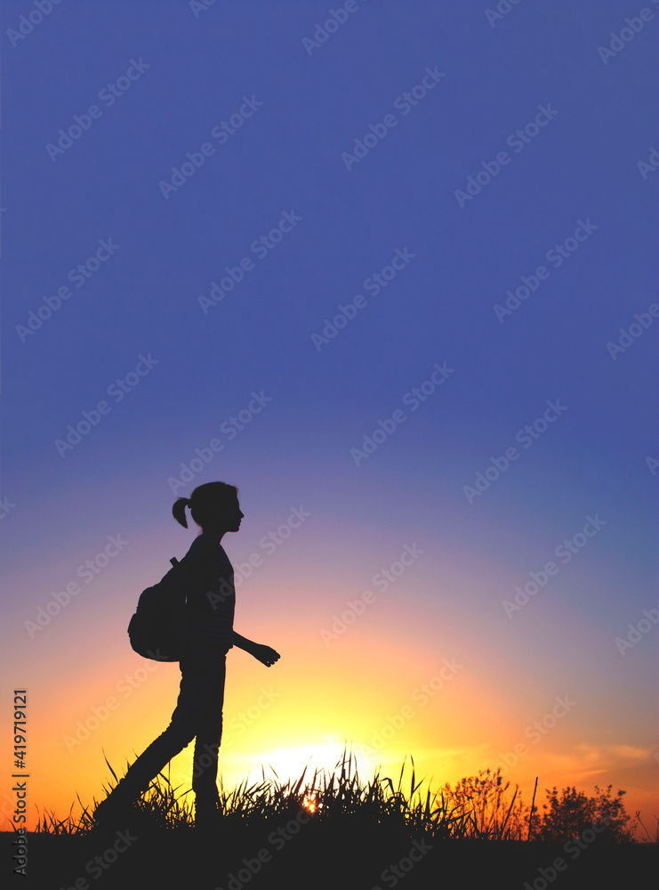 People, teens, hiking and travel concept. Silhouette of a young girl on a mountain top.Young girl with backpack enjoying sunset.Tourist traveler at sunset.
