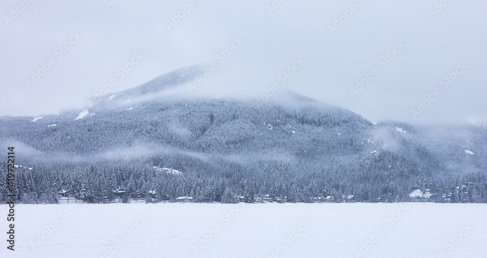 Obraz premium Beautiful View of Residential Homes in front of a frozen lake with Canadian Mountain Landscape in Background. Snowy Winter Day. Taken in Whistler, British Columbia, Canada.