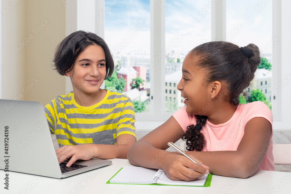 Young boy and a girl sit at a table at home and study using a laptop and the Internet Young boy and a girl sit at a table at home and study using a laptop and the Internet