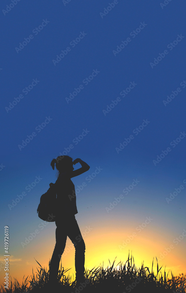 People, teens, hiking and travel concept. Silhouette of a young girl on a mountain top.Young girl with backpack enjoying sunset.Tourist traveler at sunset.