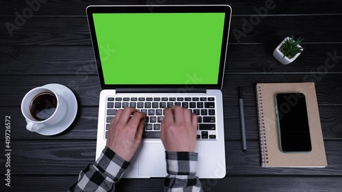 Girl's hands are typing on a green laptop screen in slow motion. View from above. Work from home, telework and selfisolation. Place a template for your text or image, advertising content. Close up. photo