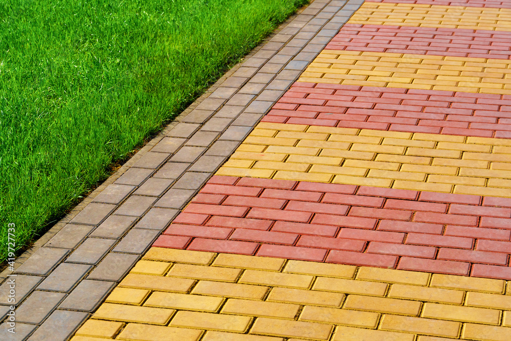 Fototapeta premium walkway made of paving slabs and green grass as a background, bright sunlight
