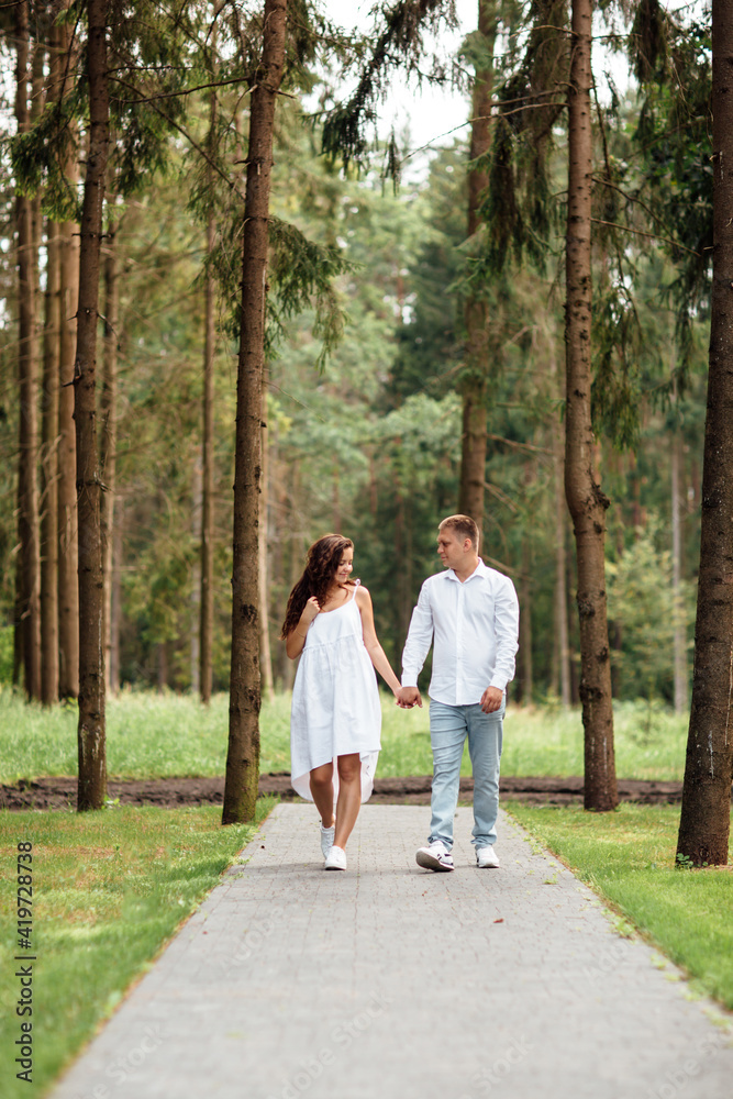 Cheerful couple in love spends time together, they walk through the woods on a summer sunny day Cheerful couple in love spends time together, they walk through the woods on a summer sunny day