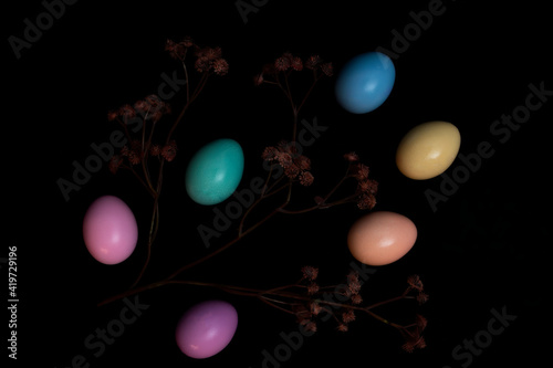 Pastel colored eggs and small flowers with a black background.