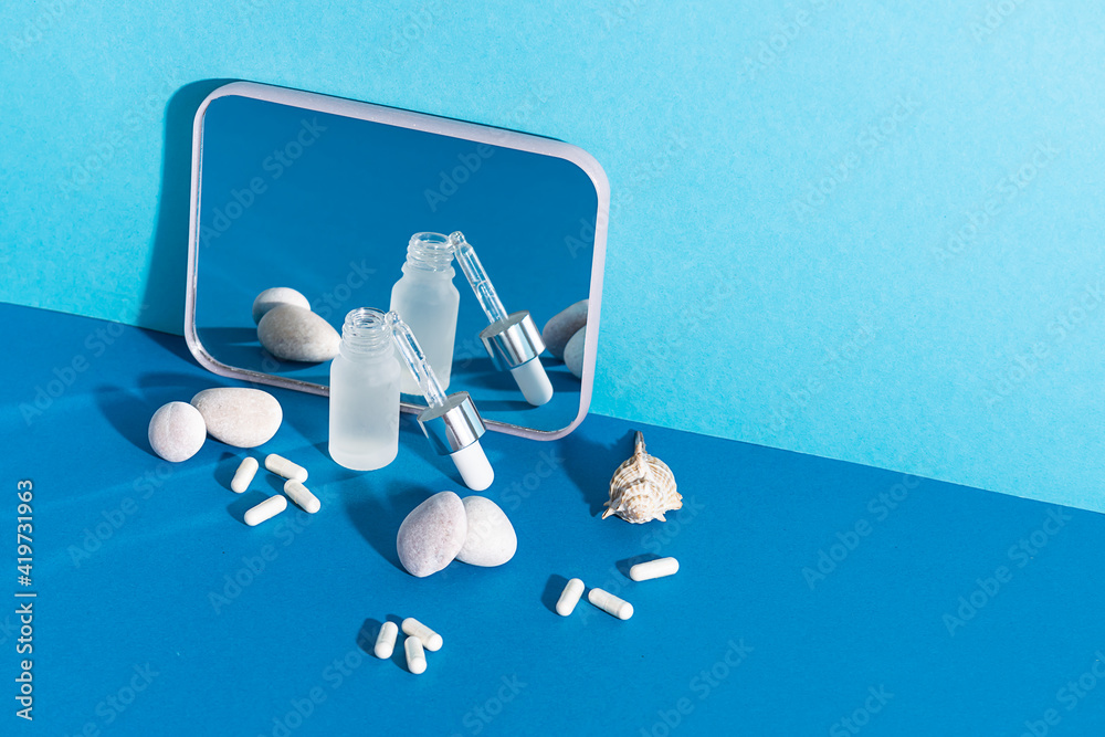 Skin care serum with sea collagen and collagen capsules on creative two tone blue background with decorative stones and mirror. Cosmetic branding banner. Copy space for your text. Skin care serum with sea collagen and collagen capsules on creative two tone blue background with decorative stones and mirror. Cosmetic branding banner. Copy space for your text.
